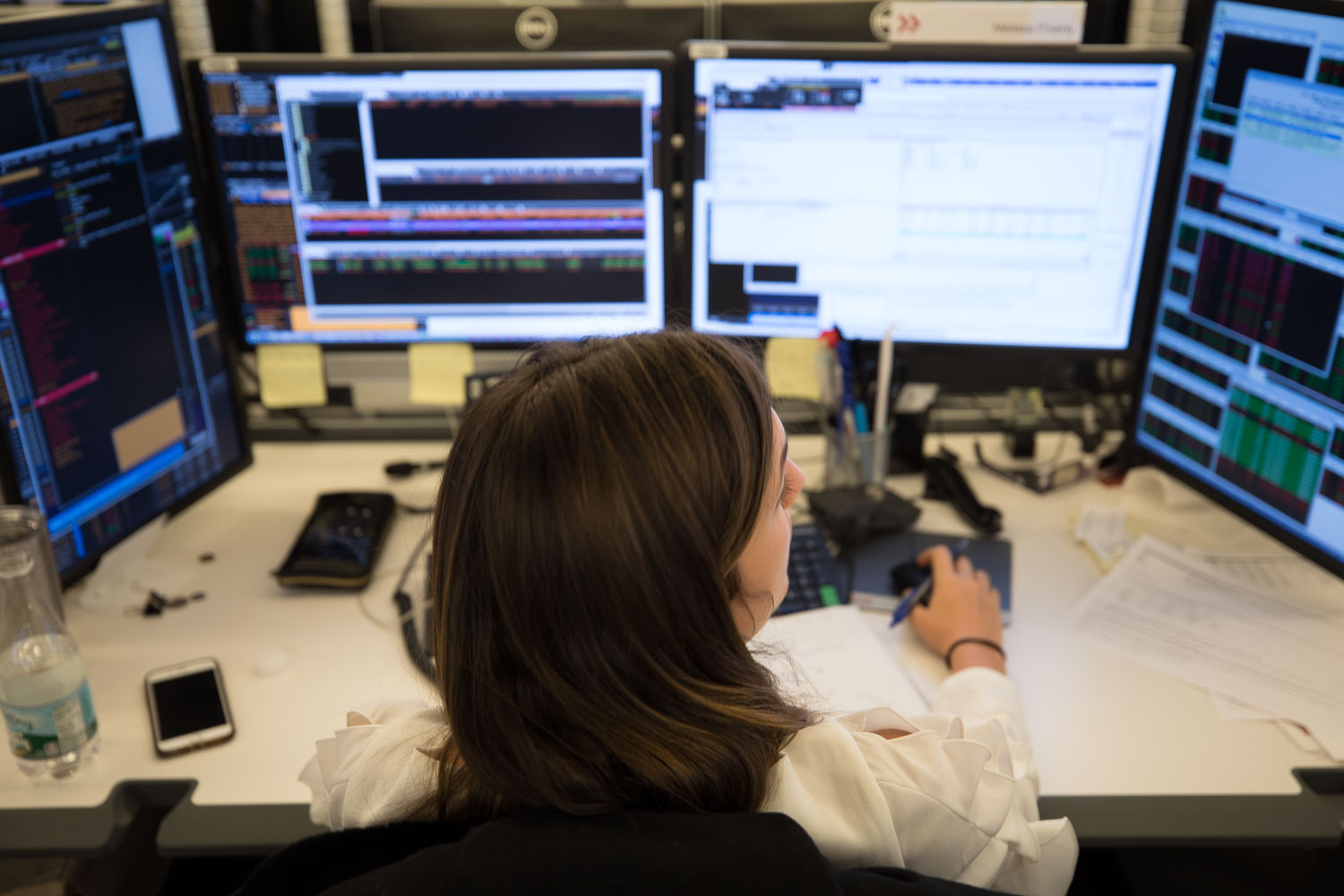 An over the shoulder view of a cluttered stock trader’s desk and multiple workstation screens.