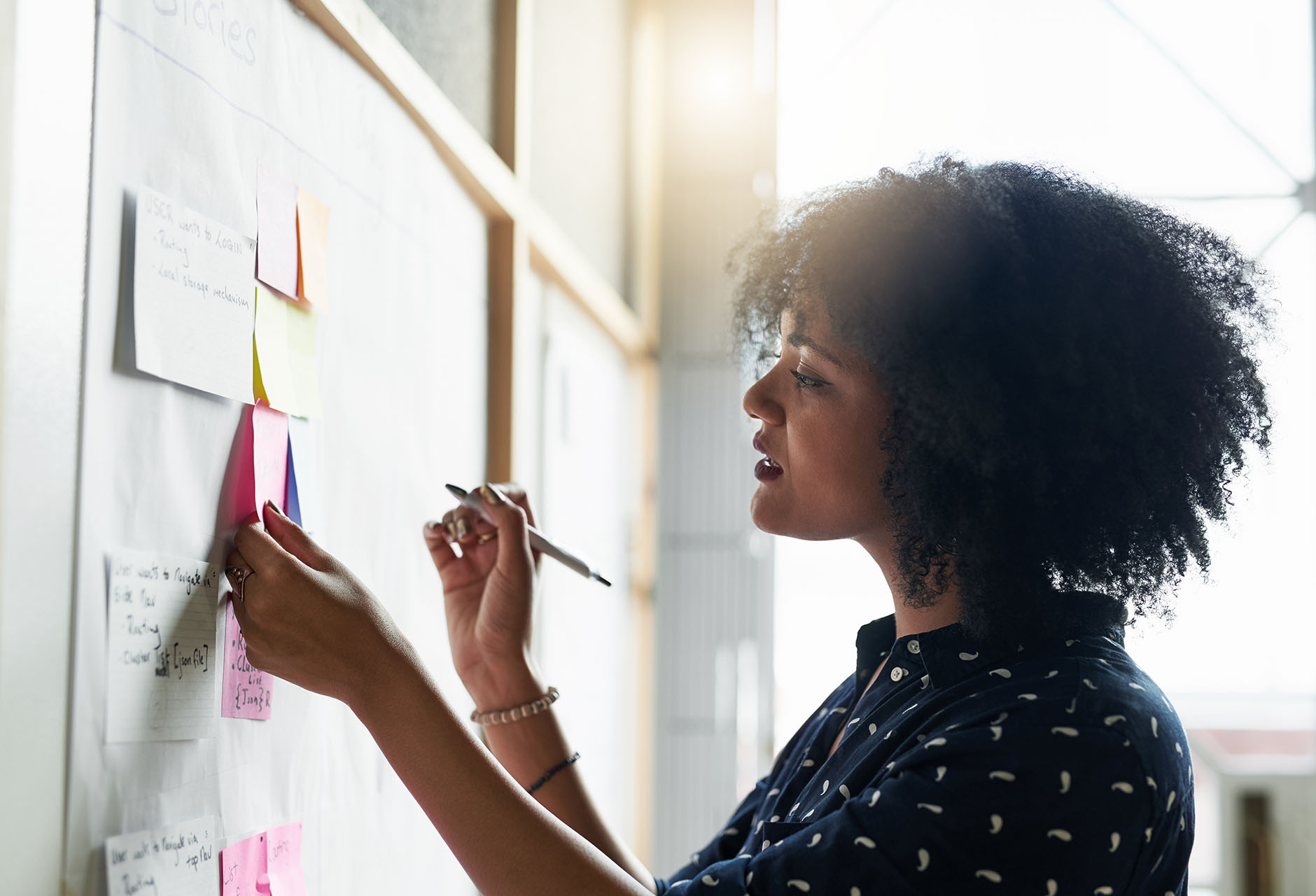 A profile view of a young woman arranging post it notes on an office wall. 