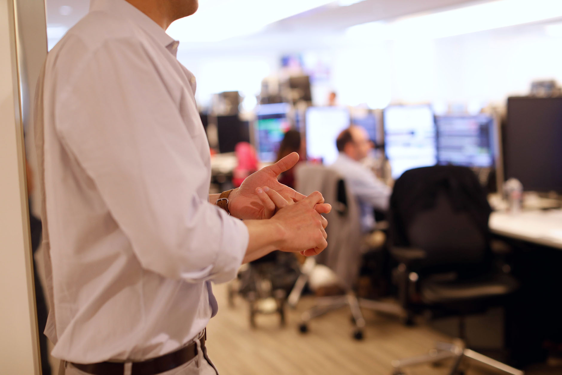 A trader gestures with his hands with a blurred view of a busy traders at their workstations in the background.